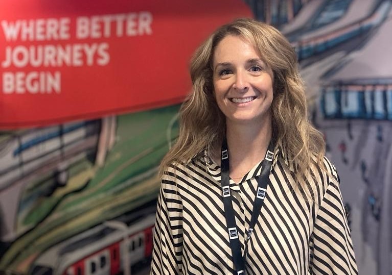 Jennifer Jefferies stands looking at the camera and smiling. She stands in front of a SYSTRA promotional banner that reads 'where better journeys begin'.