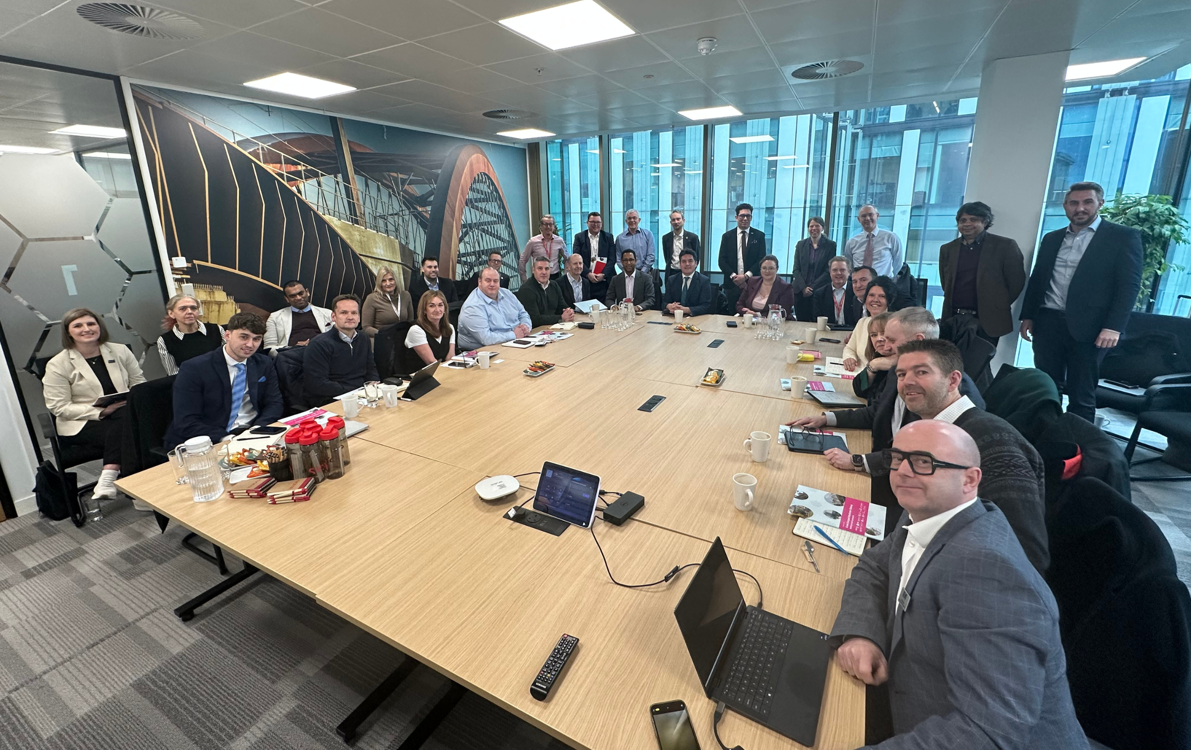A photo of the RIA meeting attendees around a large table in a meeting room in the SYSTRA Manchester office. They have all turned round and are looking at the camera.