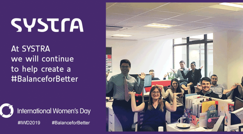 On the left, the SYSTRA logo on a purple background which reads "at SYSTRA, we will continue to create a #balanceforbetter." On the right there is a photo of an office filled with smiling, mixed gender colleagues doing the gestures for International Women's Day 2019, balance for better.